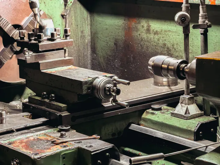 A used metal lathe on the floor of an industrial workshop